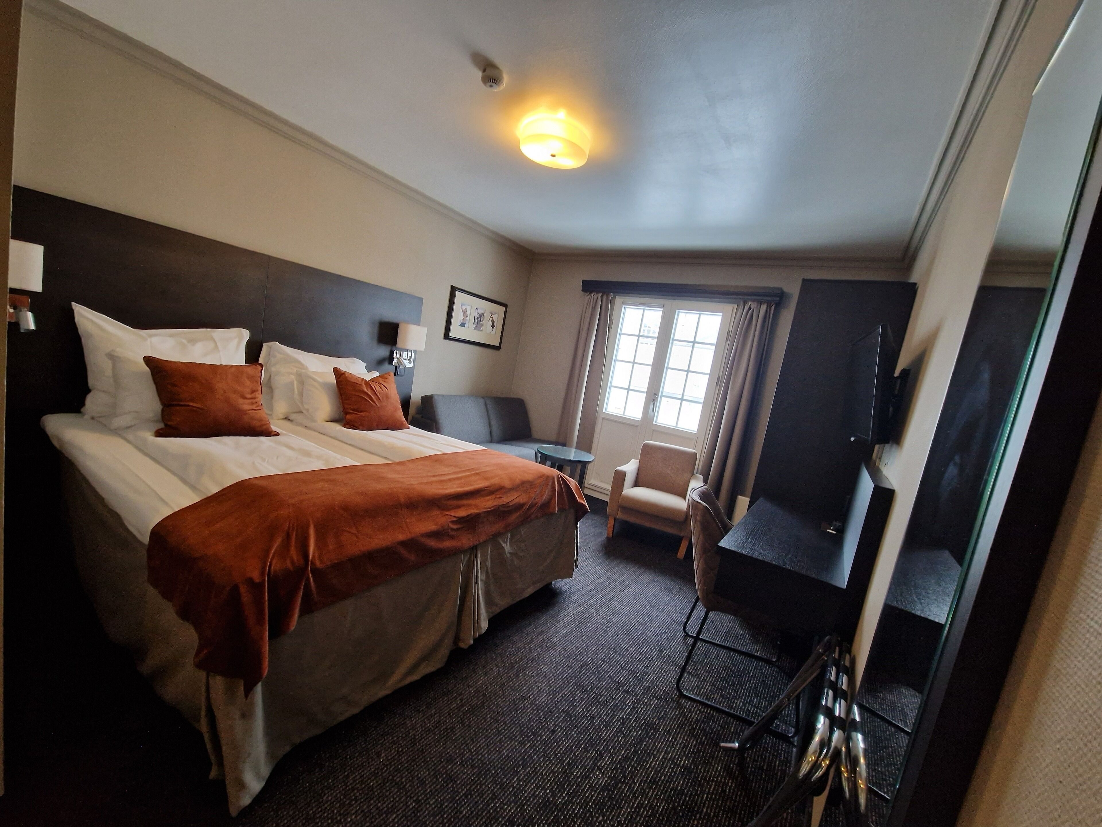 A hotel room with a large bed, a desk, a chair, and a television.