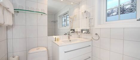 A modern bathroom with a toilet, sink, and mirror. There is a window with a view of trees and a snowy landscape.
