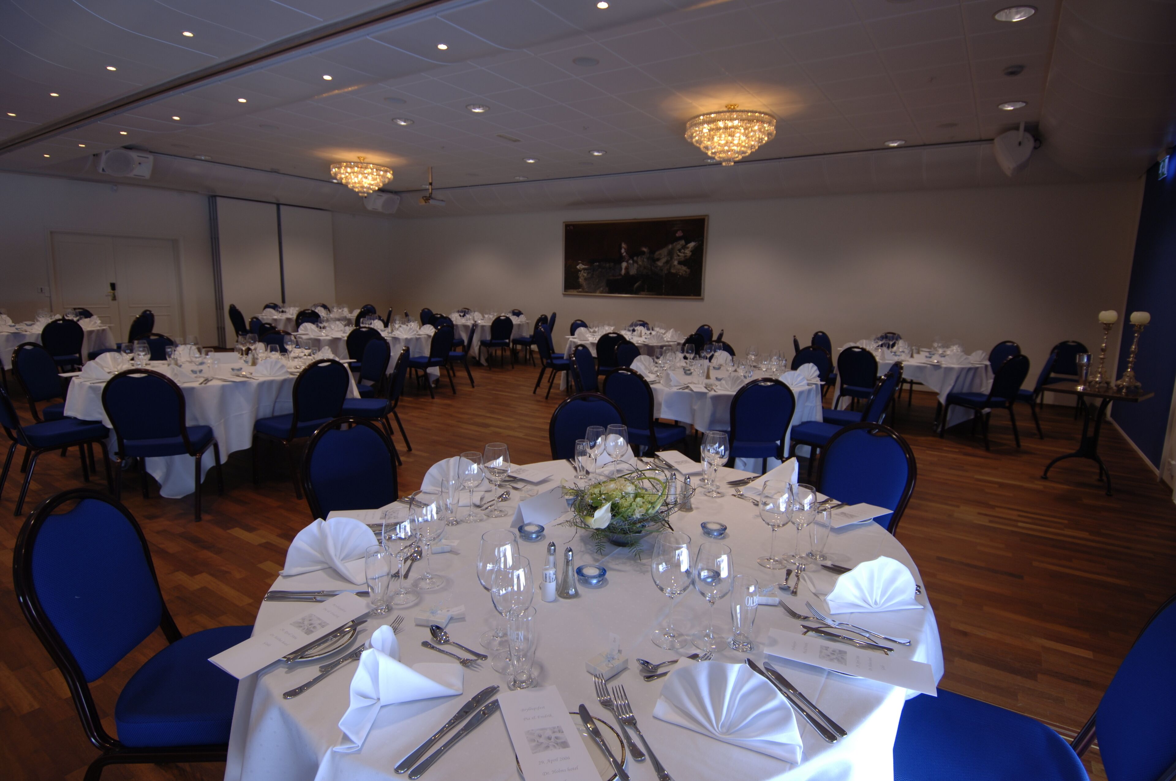 Un salón de banquetes con mesas redondas dispuestas para comer, sillas azules y candelabros.