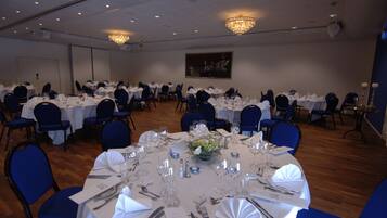 Un salón de banquetes con mesas redondas dispuestas para comer, sillas azules y candelabros.