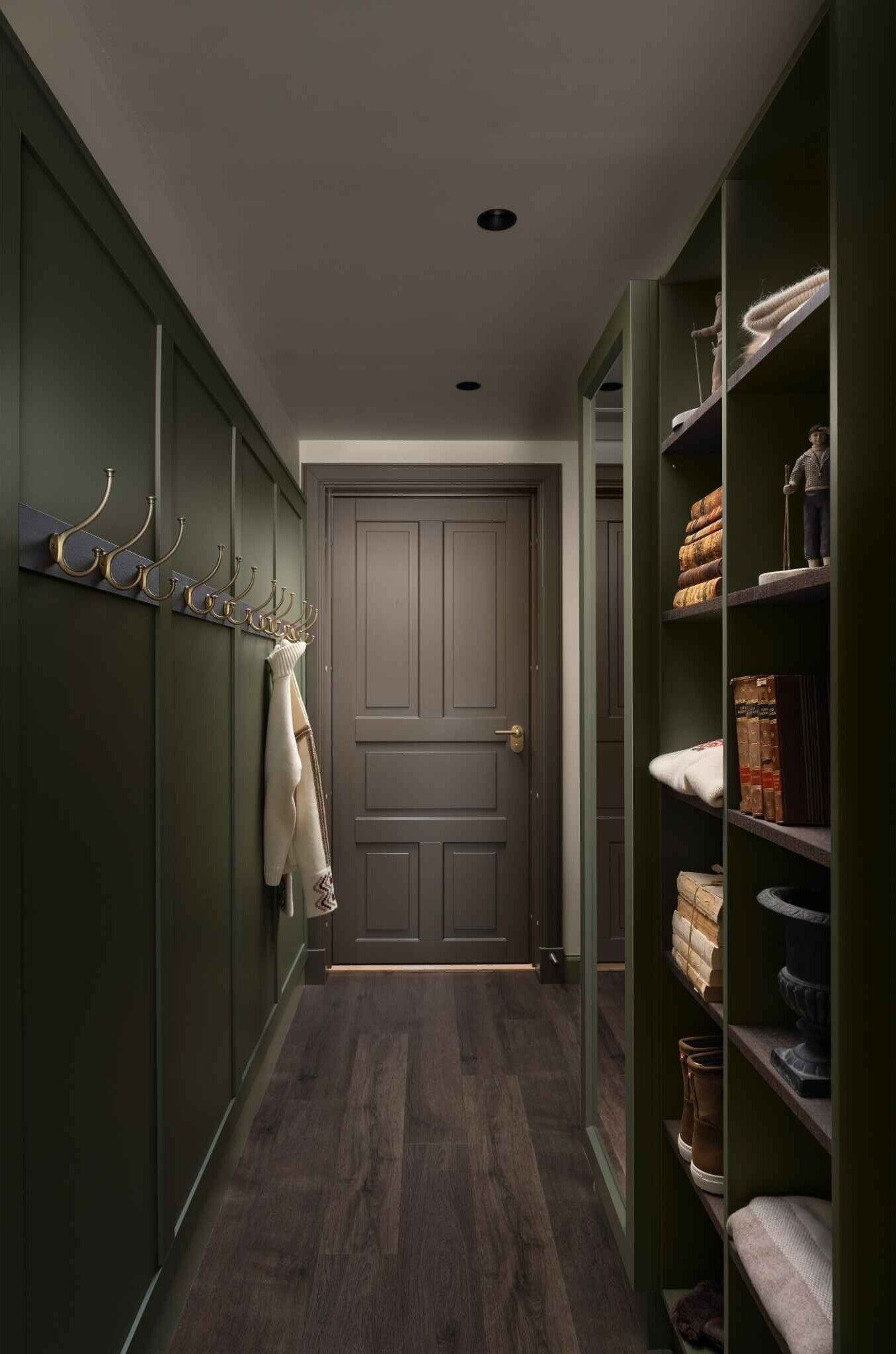 A narrow hallway with a wooden floor, a grey door, and green walls.