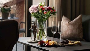 A hotel room with a dining table set with a vase of flowers, two glasses, and a plate of fruit. - Dr. Holms Hotel (Hol)