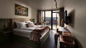 A hotel room with a bed, a television, a desk, a chair, a window with a view, and a painting on the wall. - Dr. Holms Hotel (Hol)