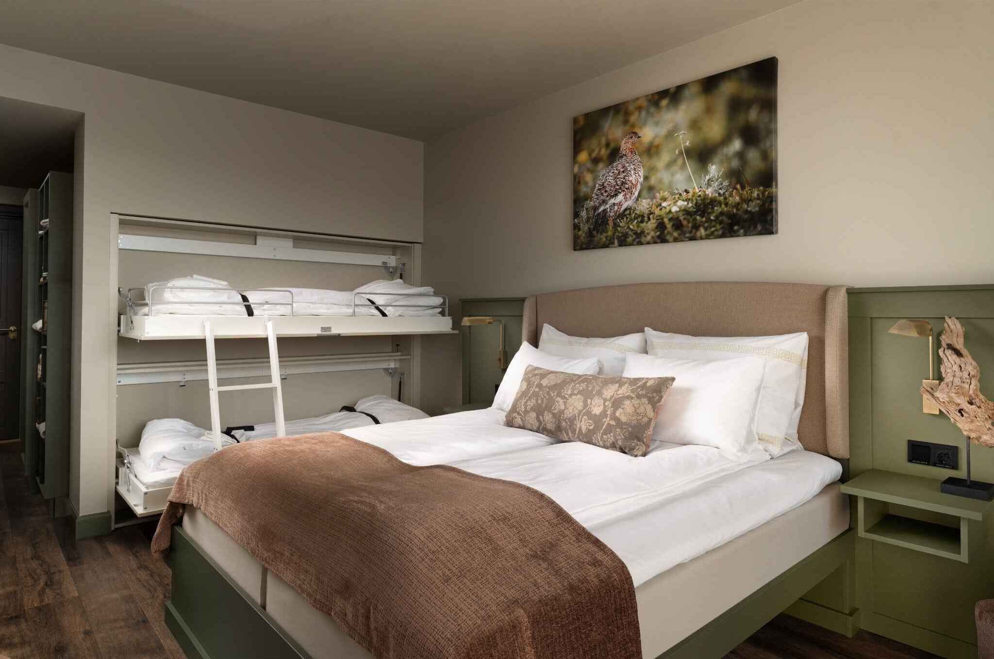 A bedroom with bunk beds, a large bed with pillows, a nightstand, and a wall-mounted artwork.