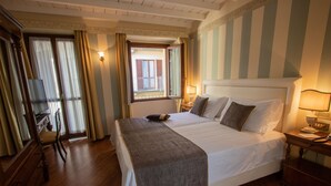 A hotel room with a large bed, wooden floor, a dresser, a mirror, and a window with curtains. - Albergo Le Due Corti (Como)
