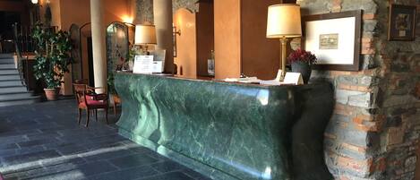 Un área de recepción con mostrador de mármol, plantas en macetas e imágenes enmarcadas en la pared.