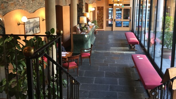 A hotel lobby with stone columns, a reception desk, a staircase, and a seating area with benches. - Albergo Le Due Corti (Como)