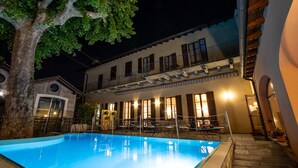 A pool area with a clear blue pool, a tree, and a building with multiple windows and balconies. - Albergo Le Due Corti (Como)