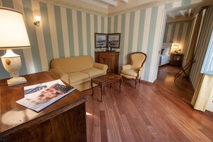 Una habitación con papel tapiz a rayas, un escritorio de madera con una revista, un sofá color beige, una silla de madera y un mueble pequeño.