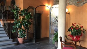 A staircase with a potted plant, a chair with a red cushion, and a wall with a decorative pattern. - Albergo Le Due Corti (Como)