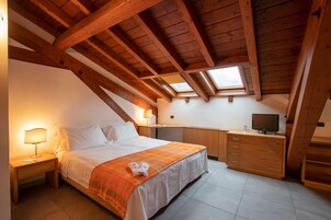 A bedroom with a bed, bedside tables, a desk, a television, and skylights.