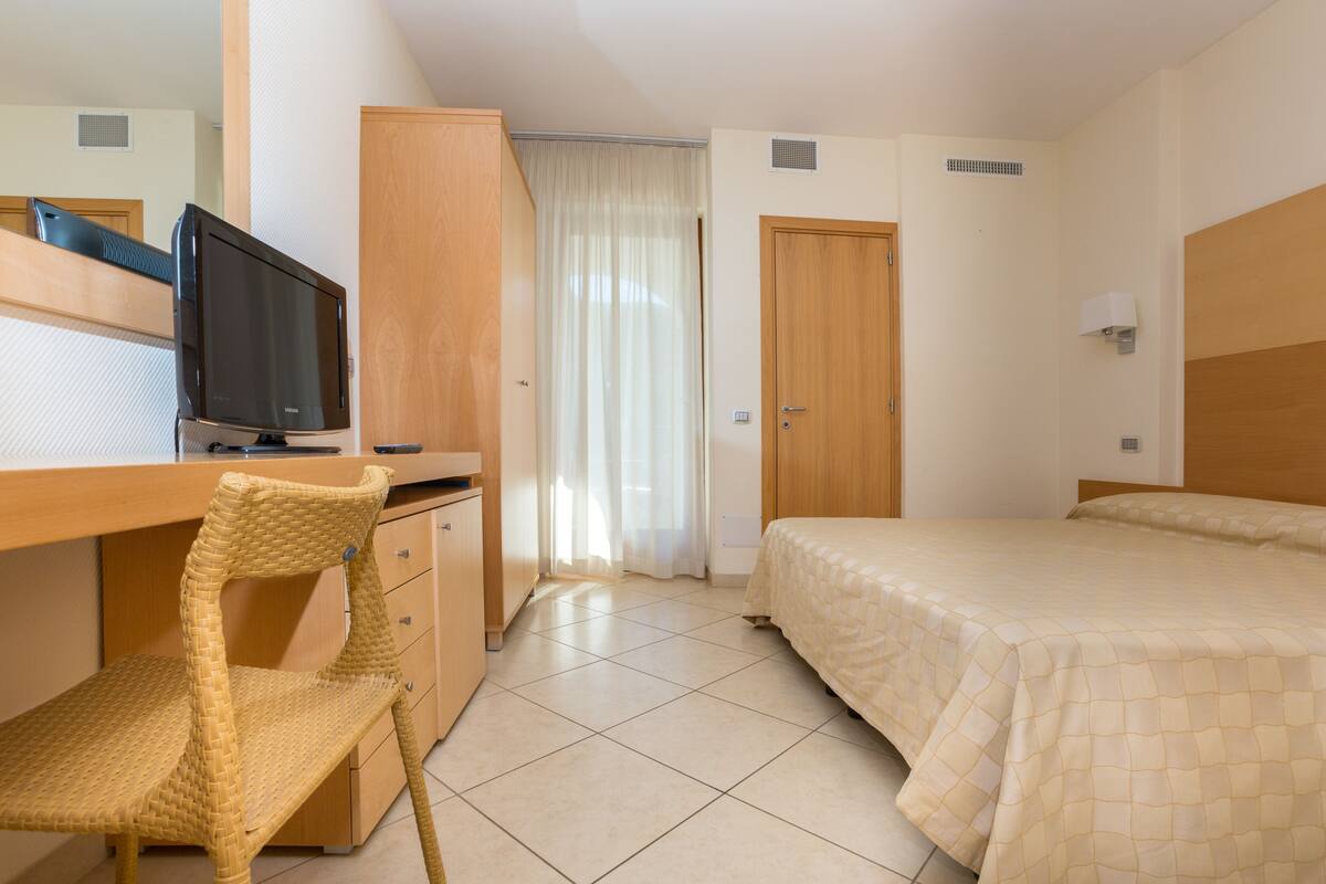 Una habitación de hotel con cama, escritorio con televisor, silla, armario y puerta.