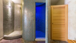 Ein Badezimmer mit einer Duschkabine mit Mosaikfliesen, einer Holztür und einem gefliesten Boden.
