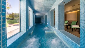 Ein Wellnessbereich mit blau gefliestem Boden und Wänden, einem Fenster und einer Sitzecke mit grünen Stühlen.