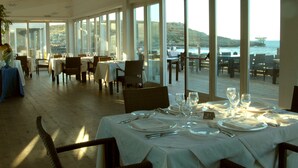 Ein Restaurant mit gedeckten Tischen, großen Fenstern mit Meerblick und einer Holzterrasse.
