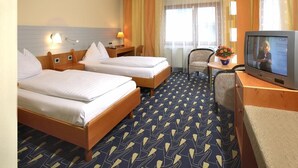 A hotel room with two beds, a desk with a television, a chair, and a small table with a flower.