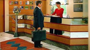 A reception desk with a man and woman standing, a plant, and a framed picture on the wall. - Rokohof (Klagenfurt am Woerthersee)