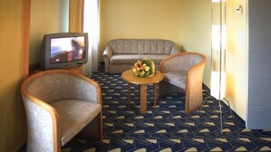 A hotel room with a sofa, two armchairs, a small table with flowers, a television, and patterned carpet. - Rokohof (Klagenfurt am Woerthersee)
