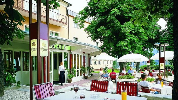 An outdoor cafe with tables and chairs, a building with a cafe sign, and potted plants.