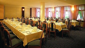 A conference room with multiple tables set for dining, chairs with cushions, and large windows with curtains. - Rokohof (Klagenfurt am Woerthersee)