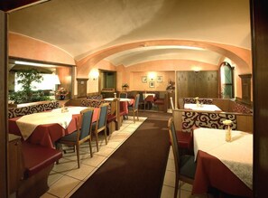 A restaurant with booths and tables, a tiled floor, and a warm color scheme. - Rokohof (Klagenfurt am Woerthersee)