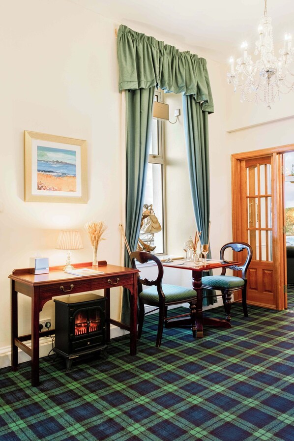 A room with a plaid carpet, a wooden table with chairs, a fireplace, a chandelier, and a door with glass panels. - Muthu Queens Hotel (Oban)