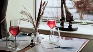 Una mesa de comedor con dos copas de vino, un florero con plantas secas y una estatua de mujer.
