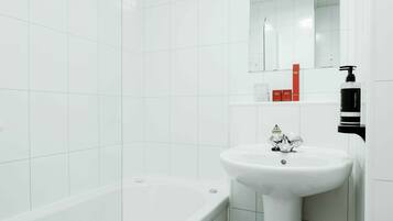 A modern bathroom with white tiles, a white bathtub, a white sink, and a mirror above the sink.