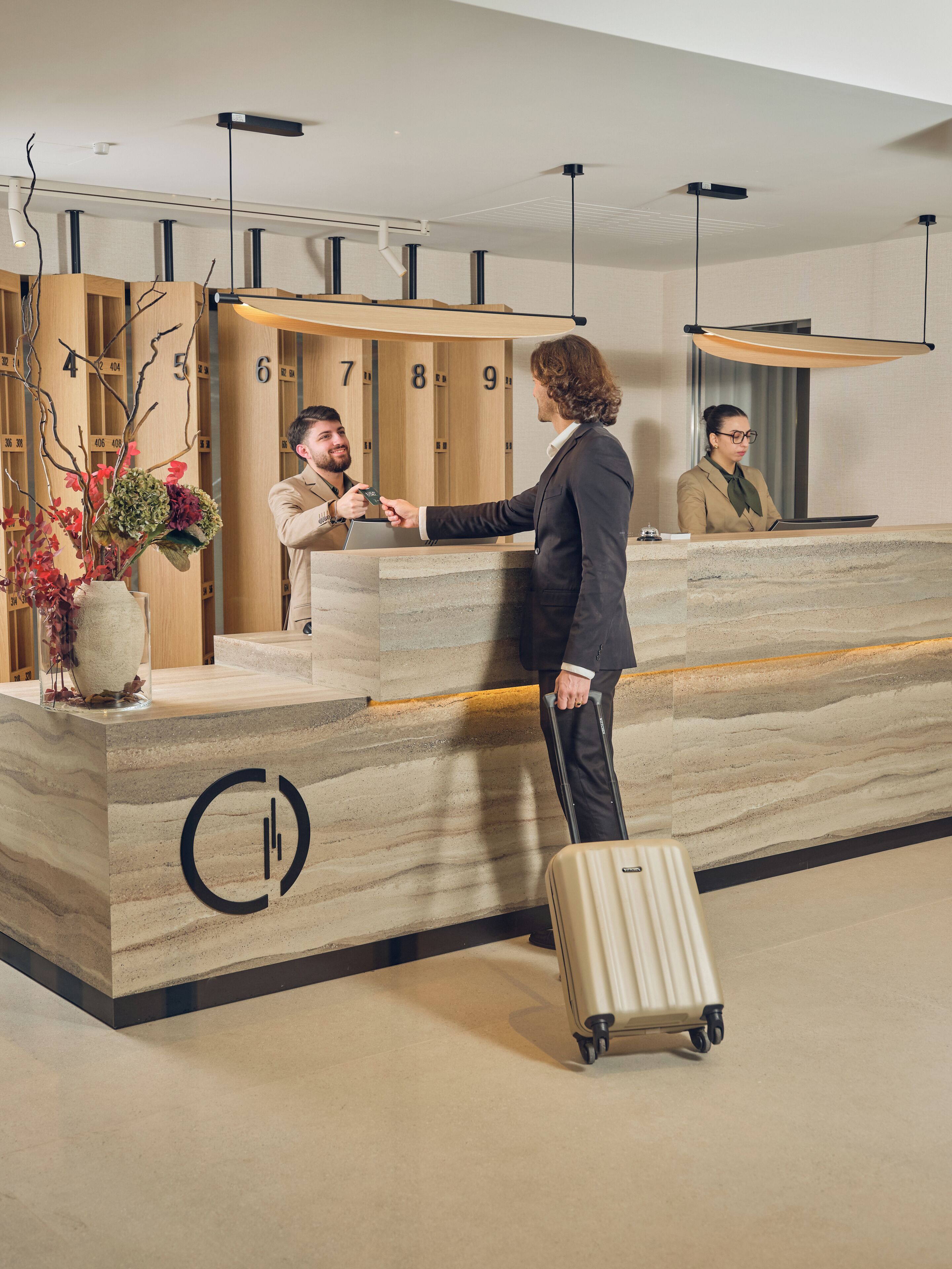 Ein Hotelrezeptionstresen mit einer Marmorplatte, einer großen Vase mit Blumen und einem Gepäckwagen.