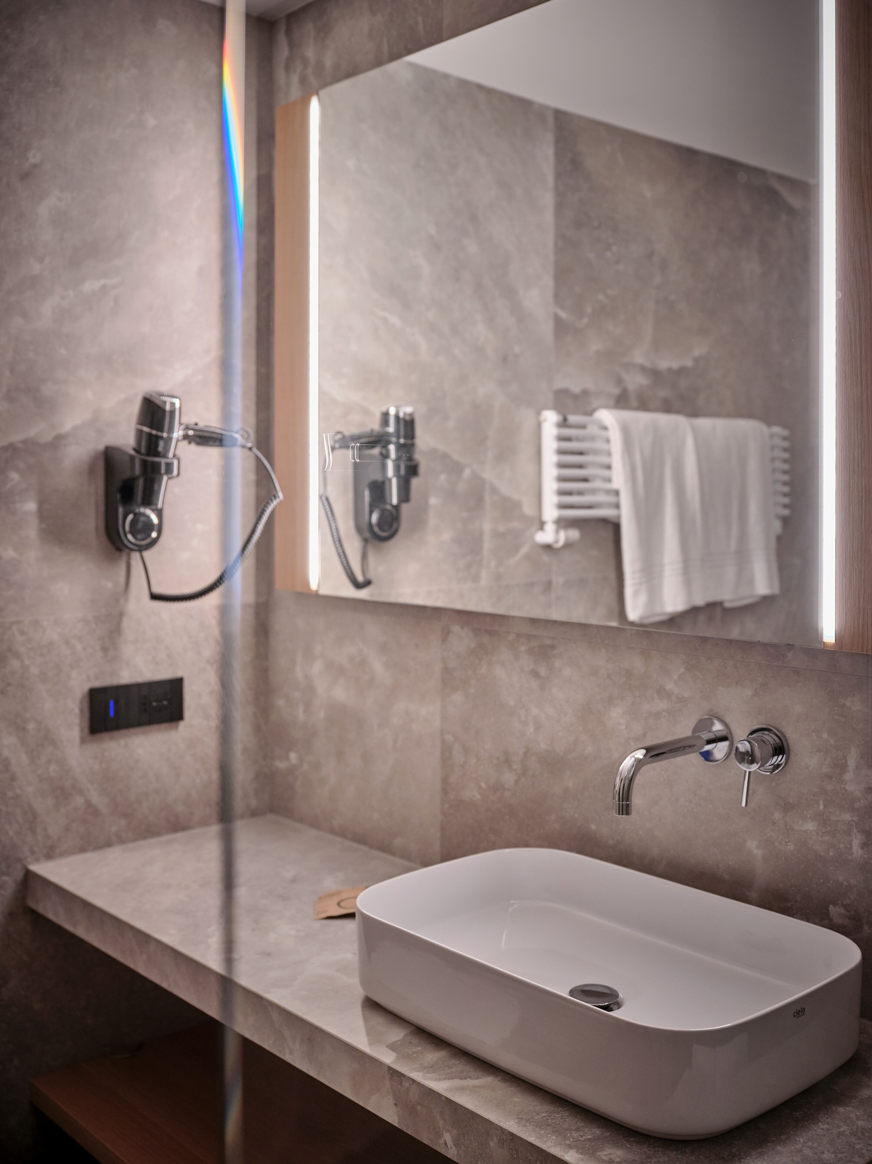 A modern bathroom with a rectangular sink, a handheld showerhead, and a towel rack.