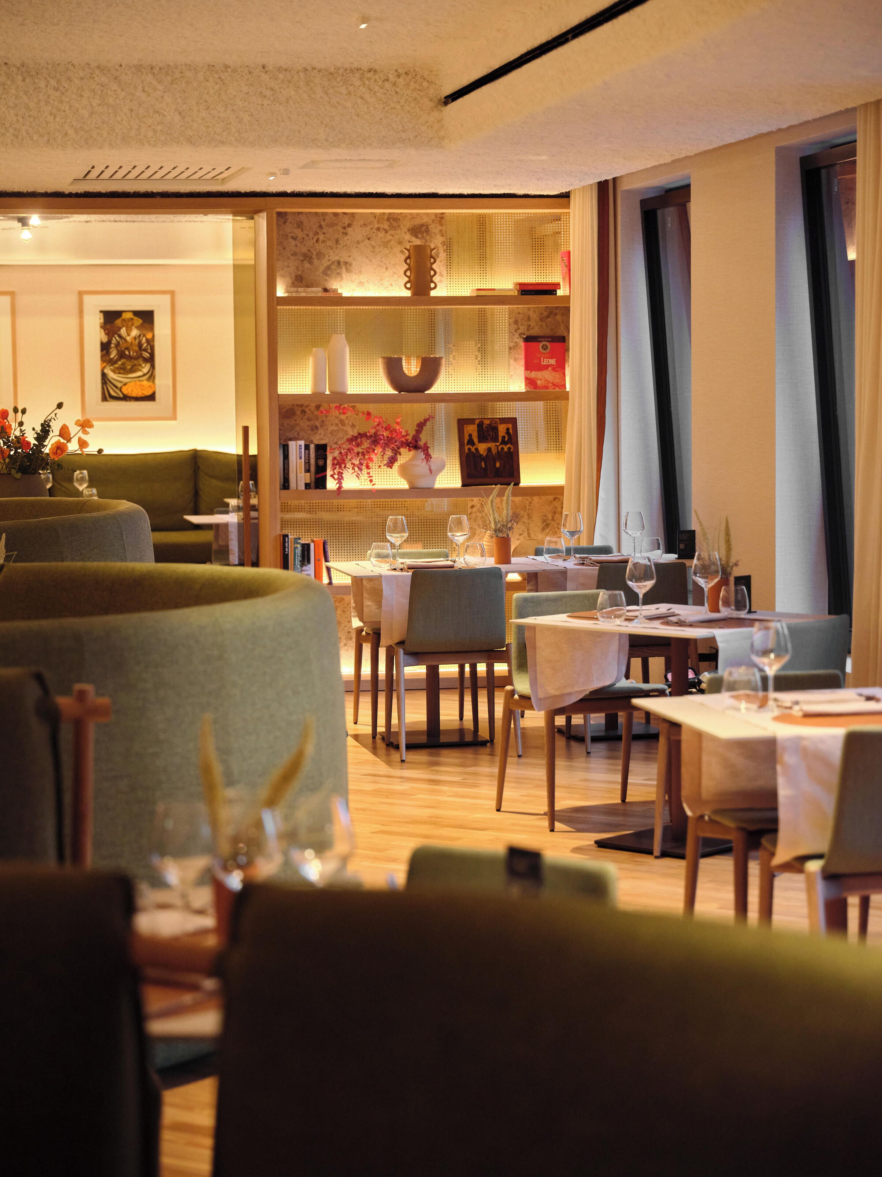 A restaurant interior with tables set for dining, chairs, and a decorative wall with artwork and a vase.