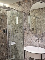 Un baño moderno con ducha envuelta en vidrio, un lavabo blanco y un espejo grande.