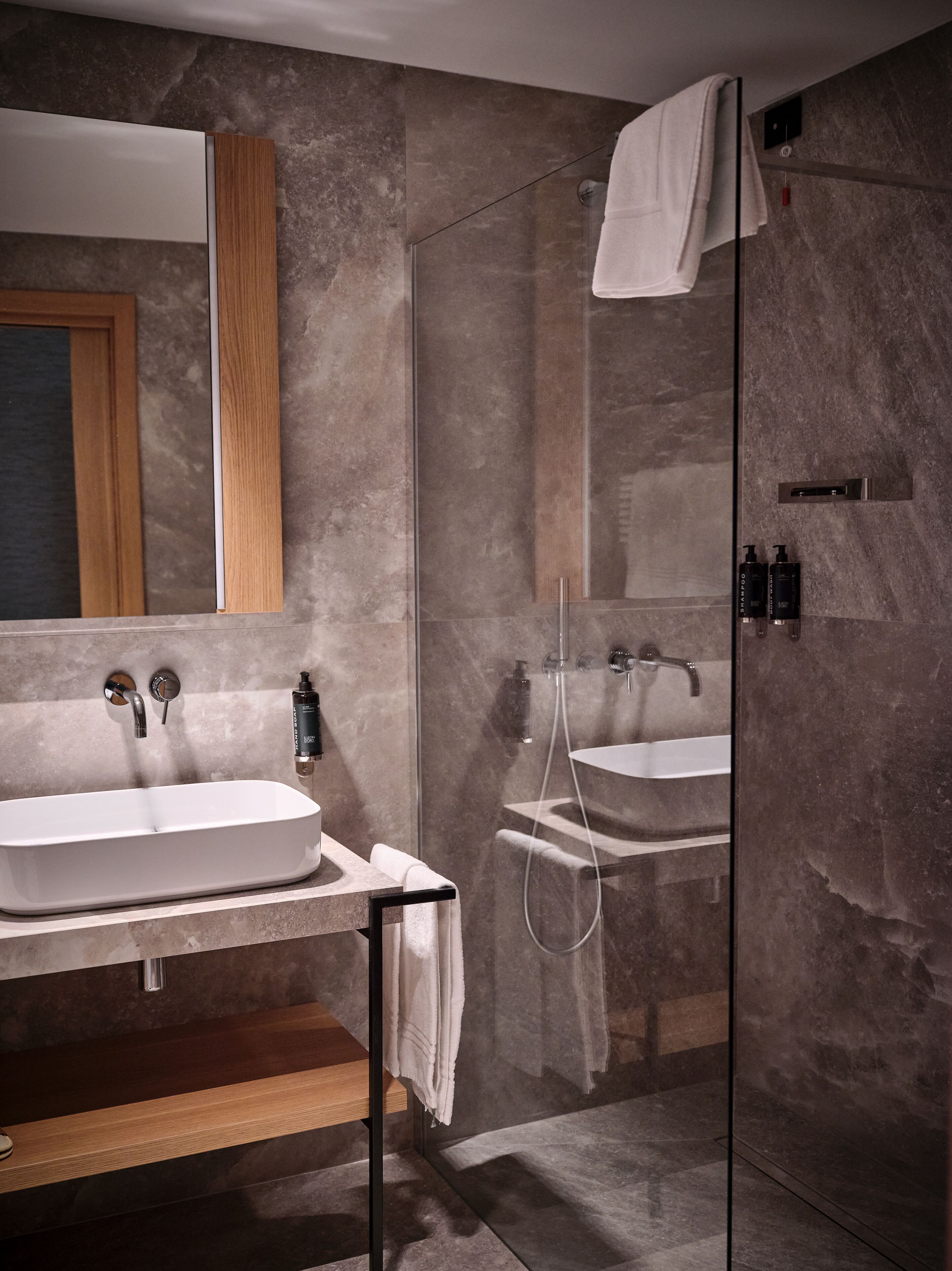 A modern bathroom with two sinks, a glass shower enclosure, and a wooden vanity.
