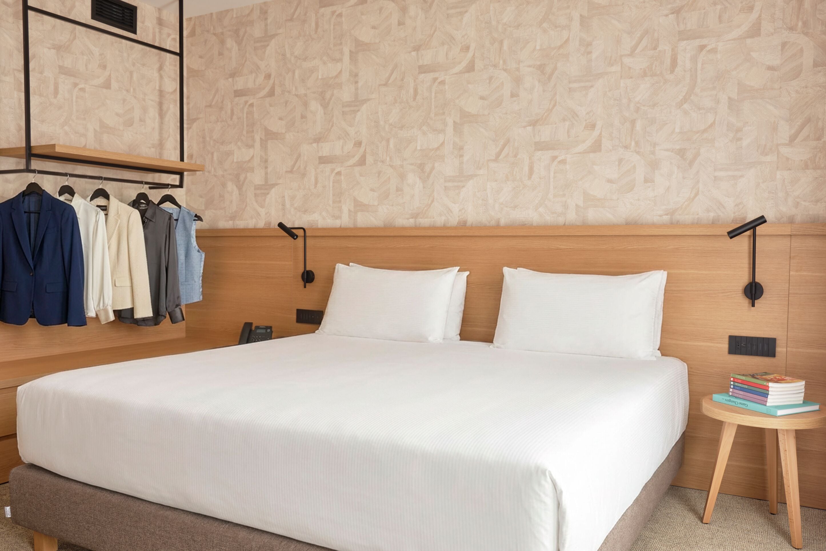 Een net opgemaakt bed met witte lakens, een houten hoofdbord en een klein nachtkastje met boeken.