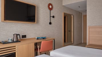 Hotellihuone, jossa on puinen työpöytä, tuoli, sänky ja suuri peili.
