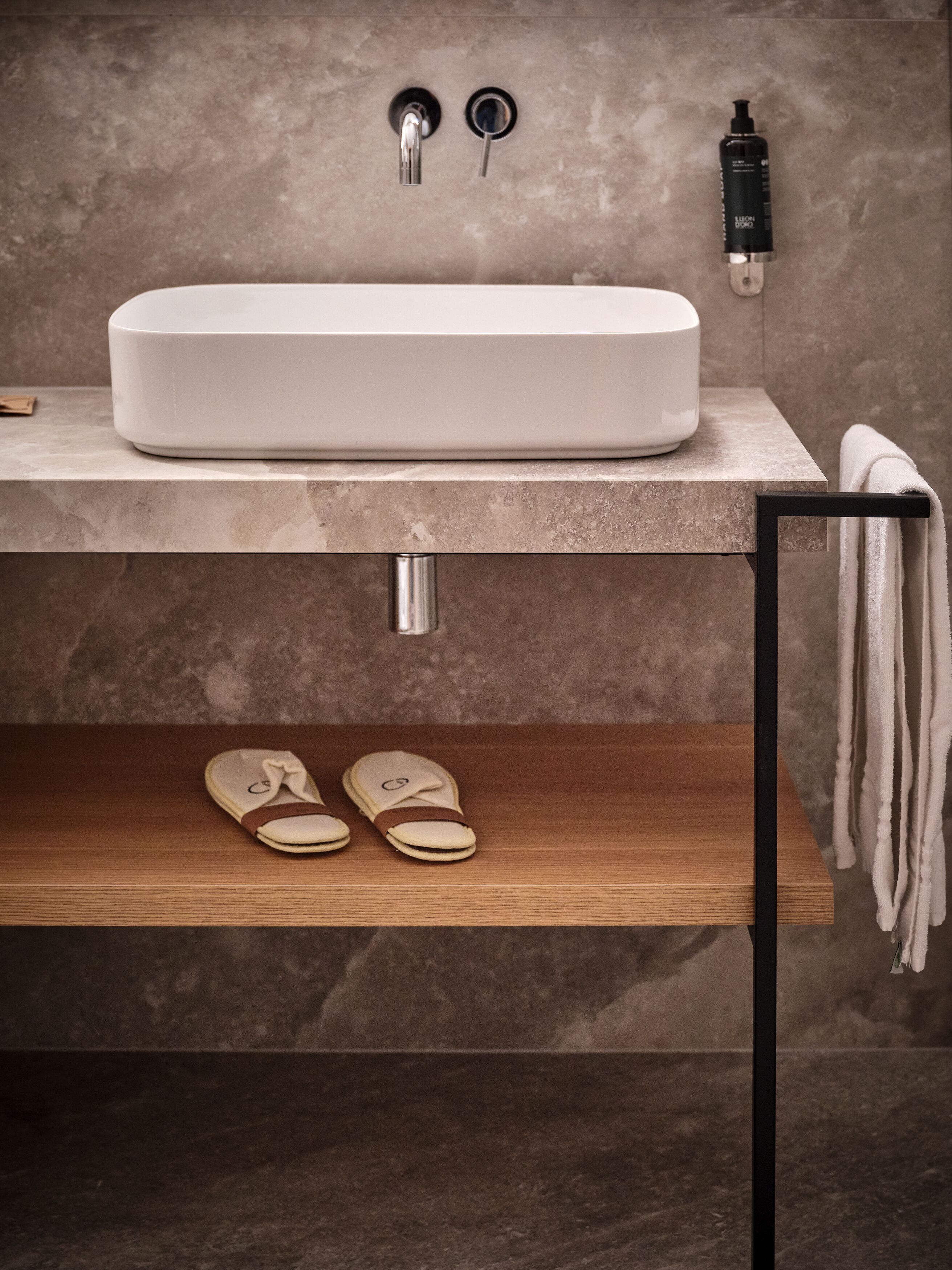Un baño con un lavamanos grande y blanco, un perchero y un estante con zapatillas.