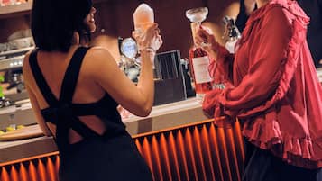 A bar area with a counter, shelves with bottles, and a person holding a drink.