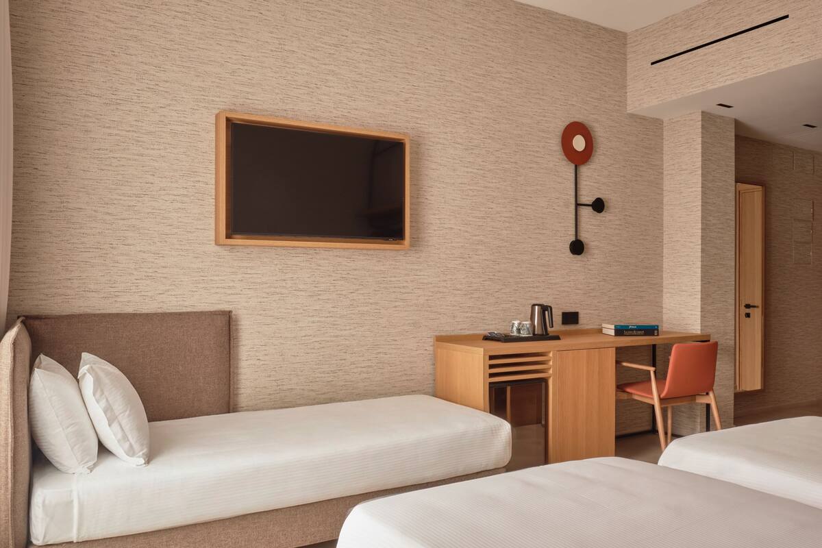 A modern hotel room with two single beds, a wooden desk, a chair, and a large mirror.