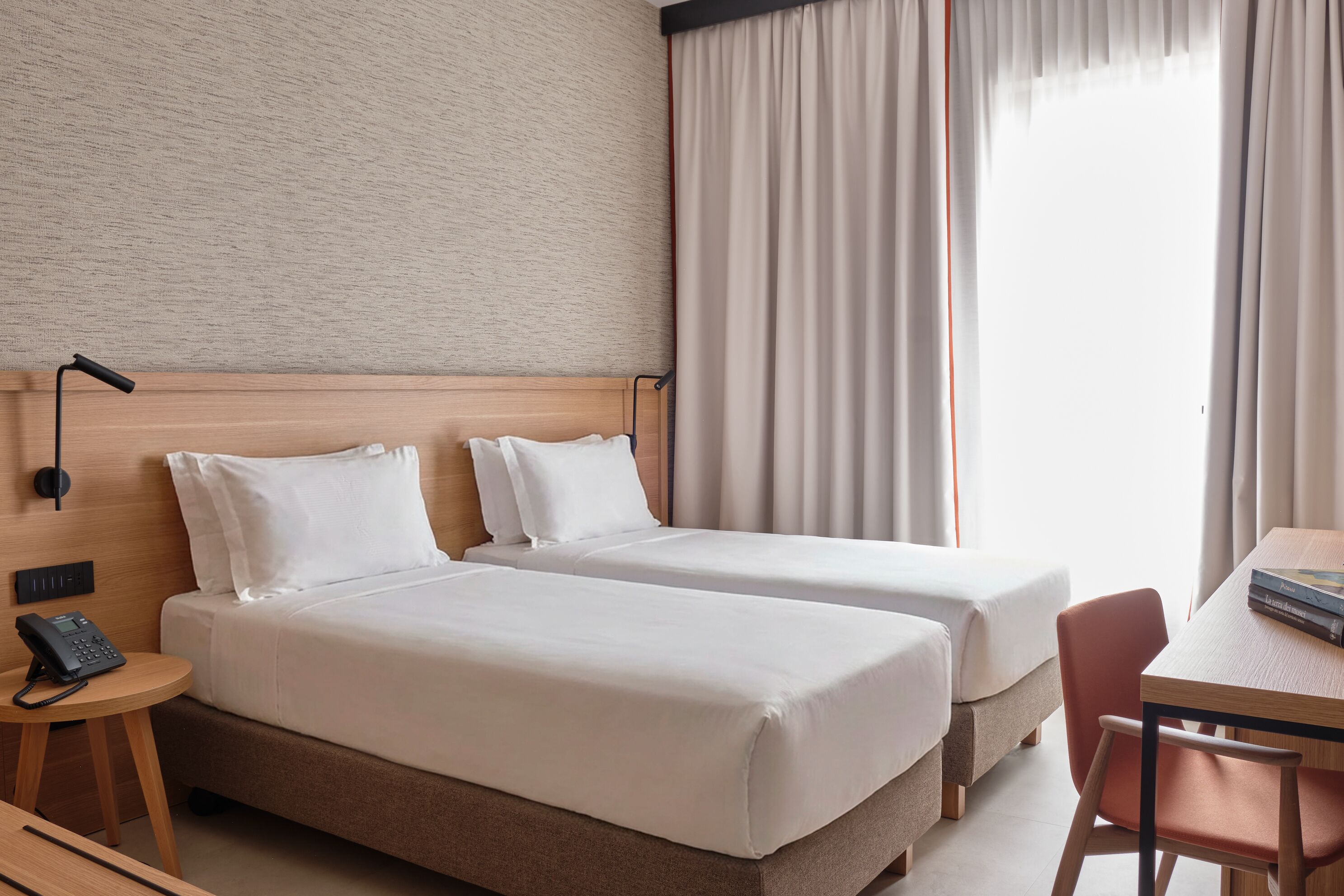 A hotel room with two beds, a desk, a chair, a phone, and a window with curtains.