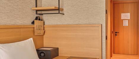 A hotel room with a wooden headboard, a bedside table with a lamp, a nightstand, and a door with a sign.
