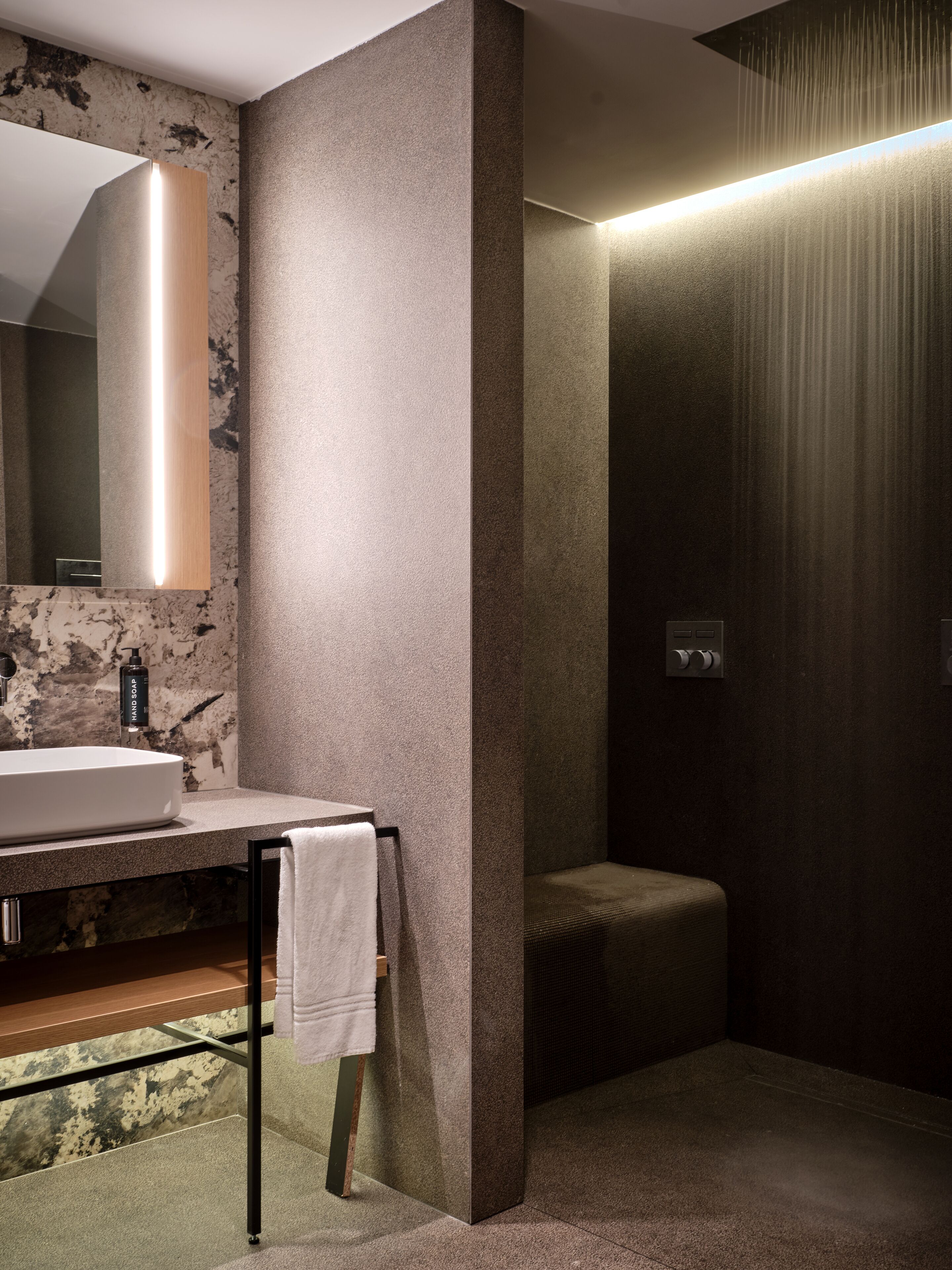 Un bagno moderno con un lavandino in marmo, un asciugamano su un portascopevoli e una zona doccia.