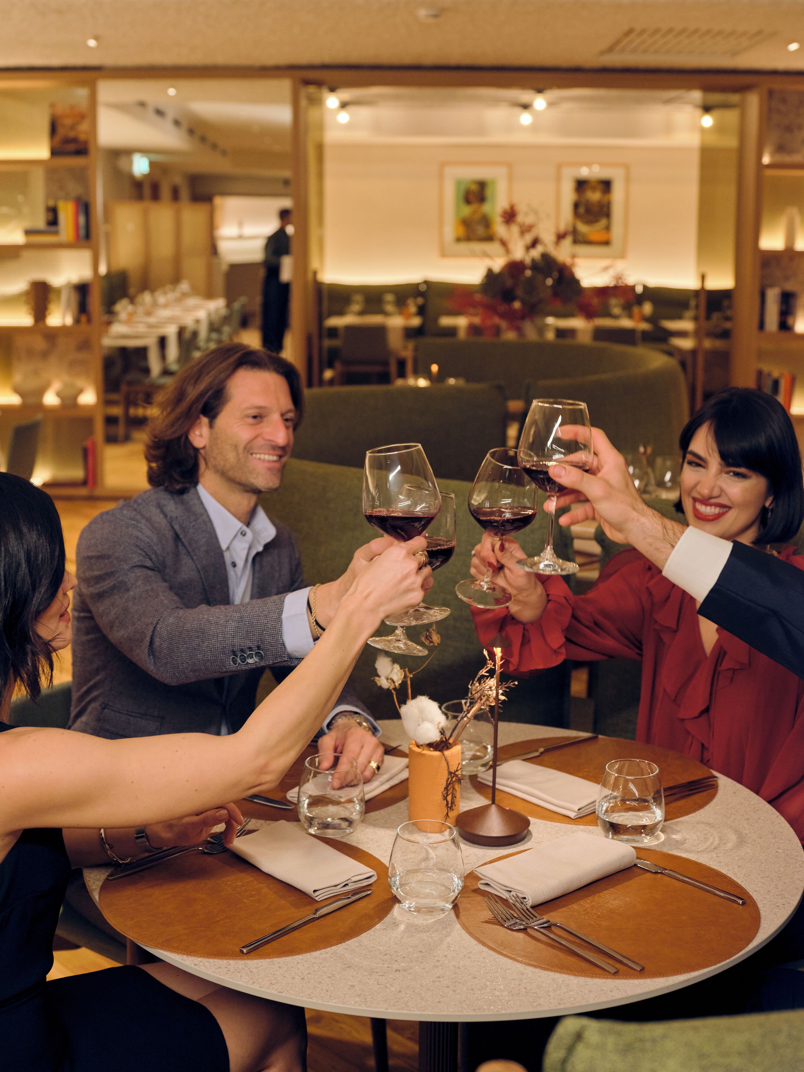 A group of people toasting with wine glasses at a round table in a restaurant setting.