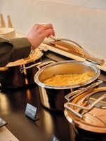 Montaje de bufé con platos etiquetados, que incluyen huevos revueltos y salchichas, y un cartel que indica el tipo de comida.