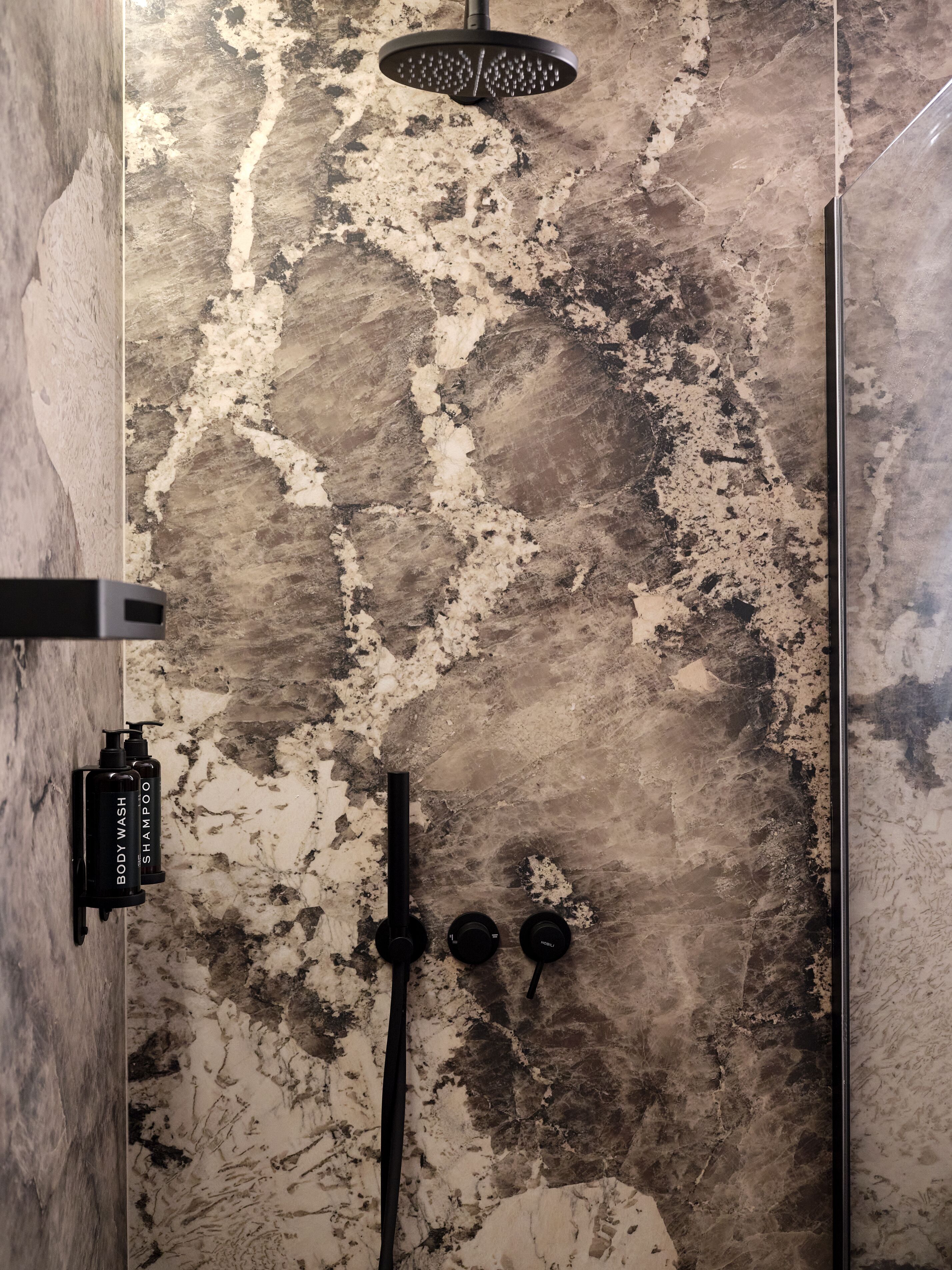 Un baño con suelo de mármol, un cabezal de ducha y dos botellas de gel de baño y champú.