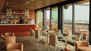 A modern bar area with a bartender, a variety of bottles, and a seating area with tables and chairs. - IL LEON D'ORO HOTEL BARI – BY FARACE HOTELS (Bari)