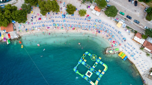 Luchtbeeld van een strand met ligbedden, parasols en een zwemgedeelte.