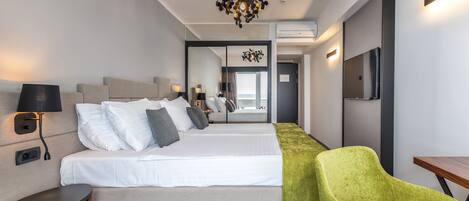 A hotel room with a bed, bedside tables, a chair, a TV, and a modern chandelier.