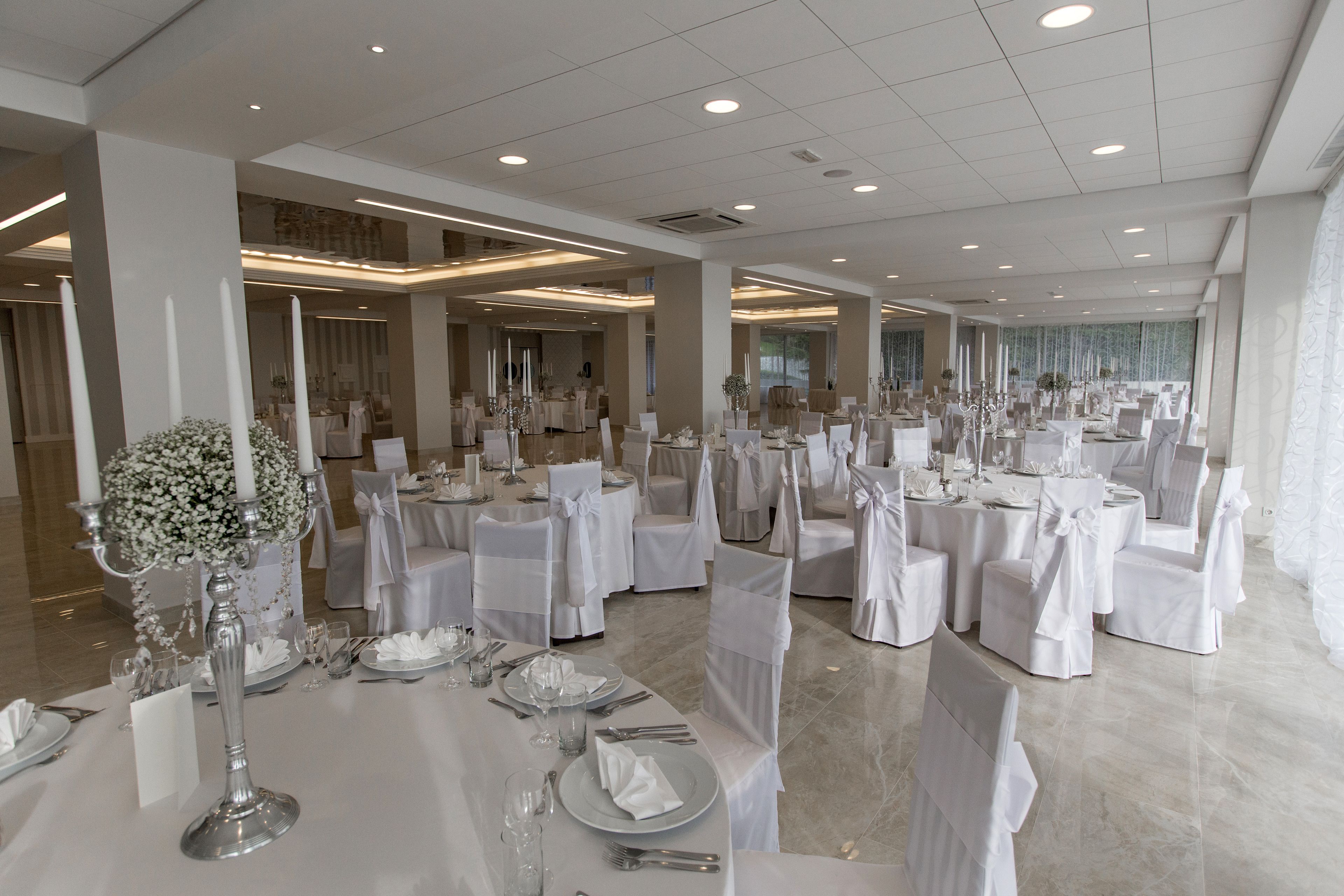 A spacious banquet hall with round tables, white tablecloths, and chairs with white sashes.