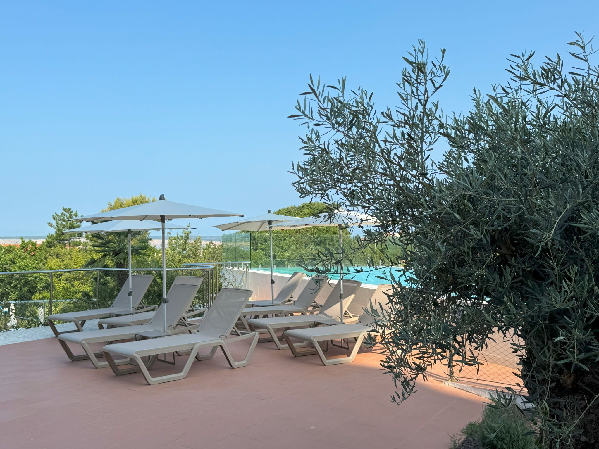 Terraza en la azotea con sillones de descanso y sombrillas, con vistas a una piscina y zonas verdes.