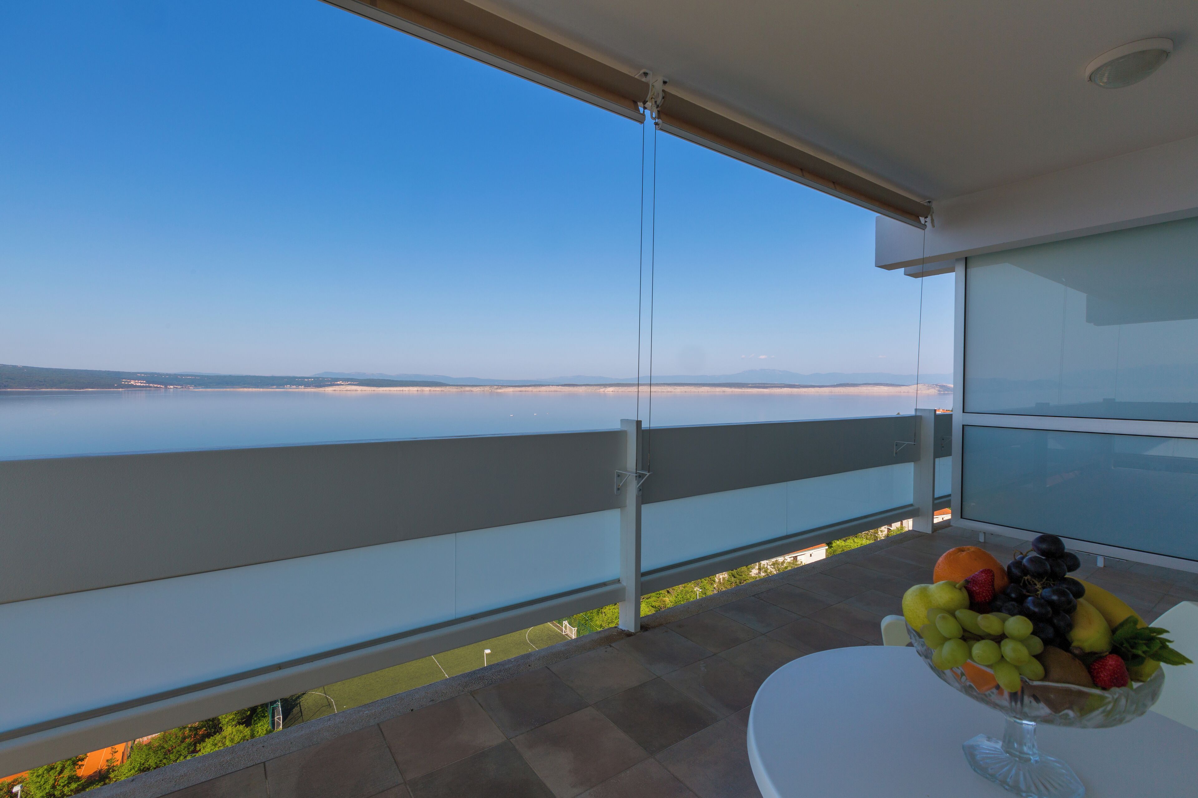 Un balcon offrant une vue dégagée sur la mer et une table sur laquelle se trouve un panier de fruits.